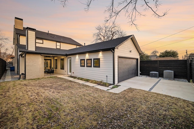 back house at dusk with central AC unit, a patio area, and a lawn