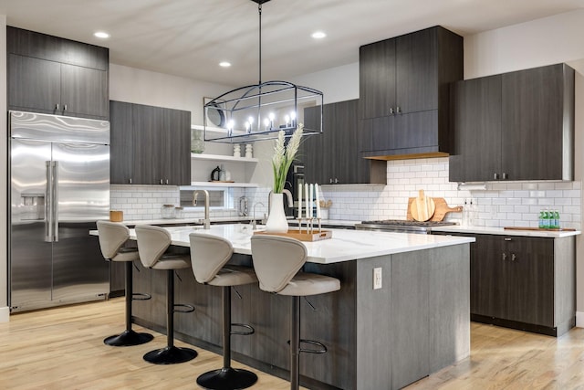 kitchen with a kitchen island with sink, decorative light fixtures, light hardwood / wood-style flooring, and built in refrigerator