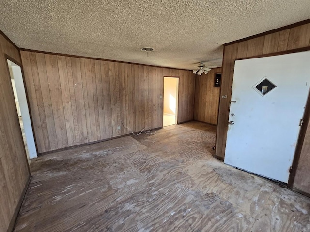 interior space with a textured ceiling, ceiling fan, and wood walls