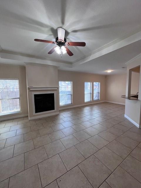 unfurnished living room with ceiling fan, crown molding, a raised ceiling, and light tile patterned floors