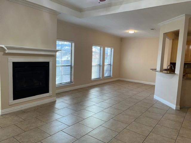 unfurnished living room with light tile patterned flooring, ceiling fan, ornamental molding, and a tray ceiling