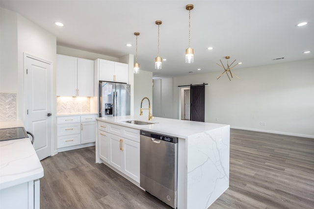 kitchen featuring appliances with stainless steel finishes, white cabinetry, an island with sink, sink, and a barn door