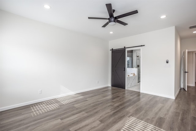 unfurnished bedroom featuring ceiling fan, hardwood / wood-style floors, ensuite bathroom, and a barn door