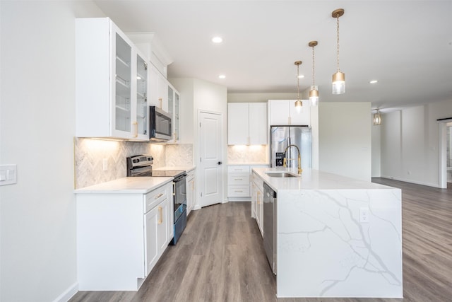 kitchen featuring white cabinets, decorative light fixtures, stainless steel appliances, an island with sink, and decorative backsplash