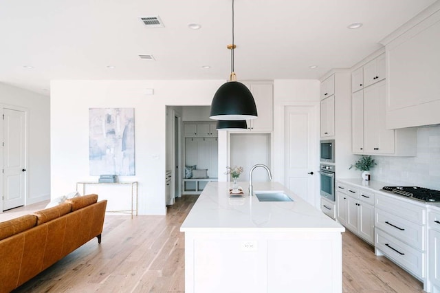 kitchen featuring sink, stainless steel appliances, light stone counters, an island with sink, and pendant lighting