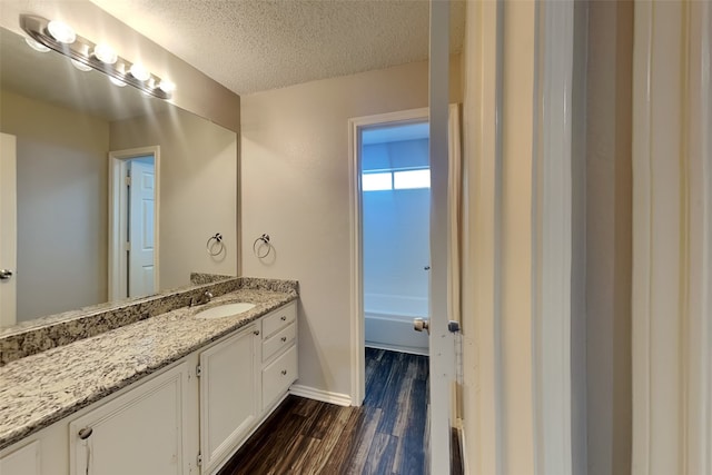 full bath featuring baseboards, wood finished floors, a bathtub, a textured ceiling, and vanity