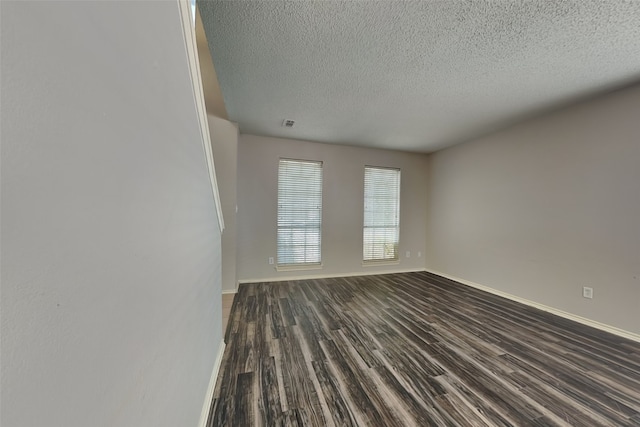 spare room featuring a textured ceiling, baseboards, and dark wood-type flooring