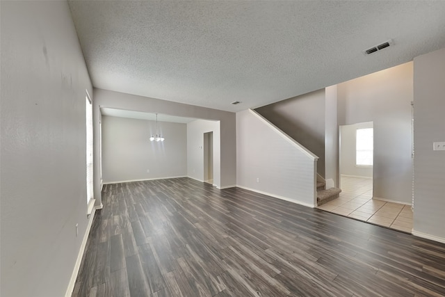 unfurnished living room featuring an inviting chandelier, a textured ceiling, and hardwood / wood-style floors