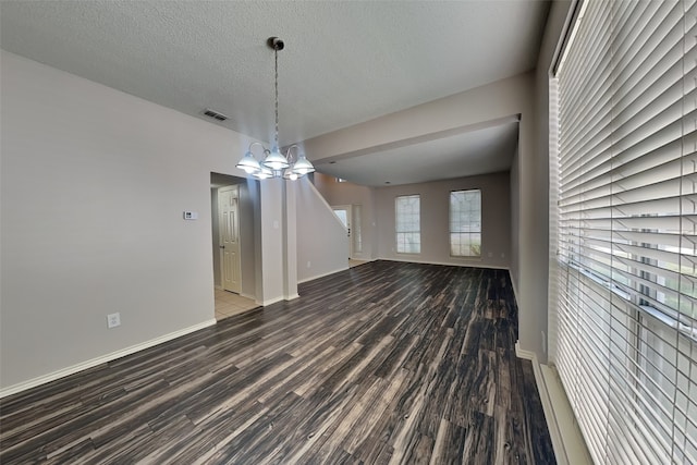 unfurnished dining area featuring a textured ceiling, a notable chandelier, and dark wood-type flooring