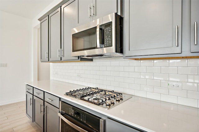 kitchen with stainless steel appliances, gray cabinets, and tasteful backsplash