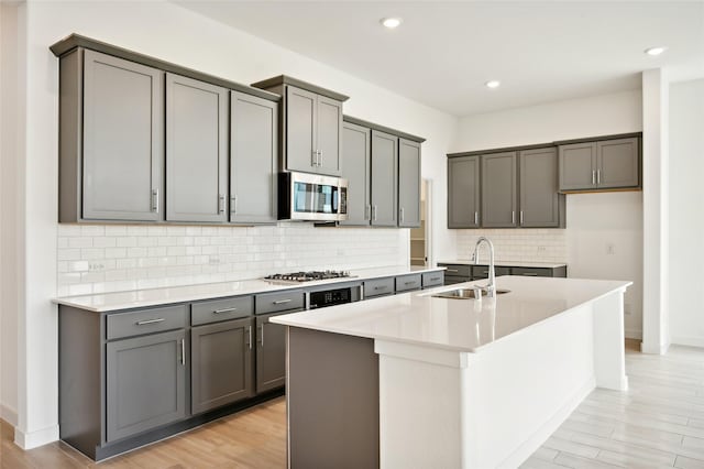 kitchen with appliances with stainless steel finishes, gray cabinets, a kitchen island with sink, and sink