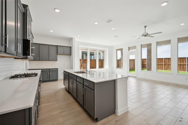 kitchen with sink, decorative backsplash, plenty of natural light, and a center island with sink