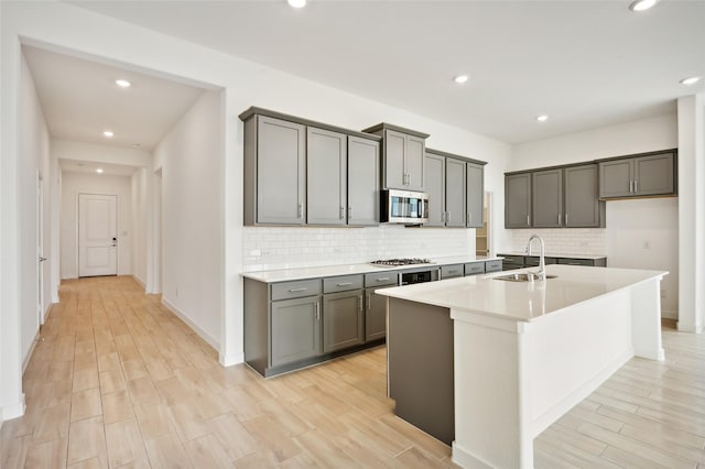 kitchen featuring appliances with stainless steel finishes, gray cabinets, a kitchen island with sink, and sink