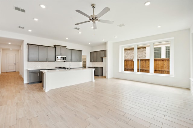 kitchen with sink, ceiling fan, light hardwood / wood-style flooring, decorative backsplash, and a kitchen island with sink