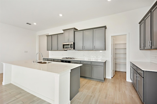 kitchen with a kitchen island with sink, appliances with stainless steel finishes, gray cabinetry, and sink