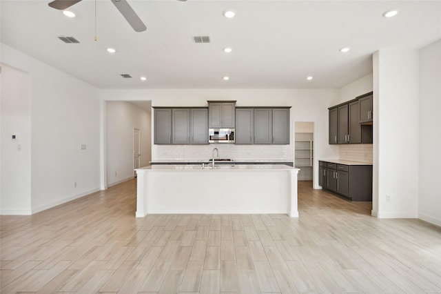 kitchen with light hardwood / wood-style floors, ceiling fan, backsplash, and a center island with sink