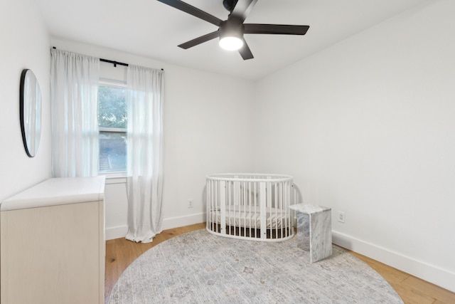 bedroom with ceiling fan, a crib, and light hardwood / wood-style floors