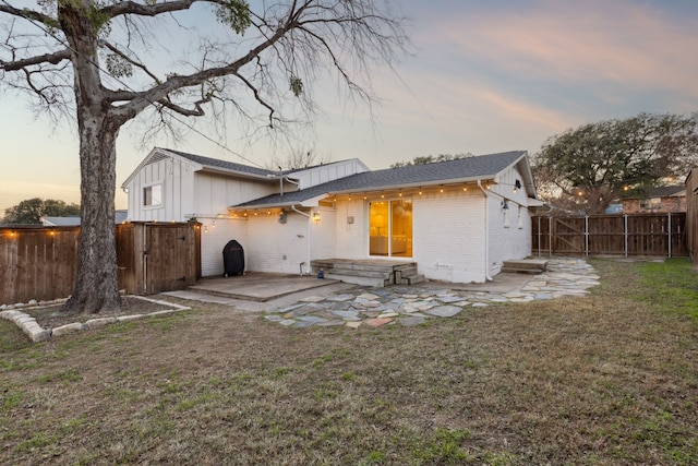 back house at dusk featuring a patio area and a lawn