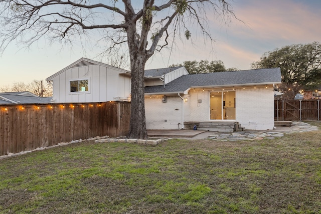 back house at dusk featuring a patio and a lawn