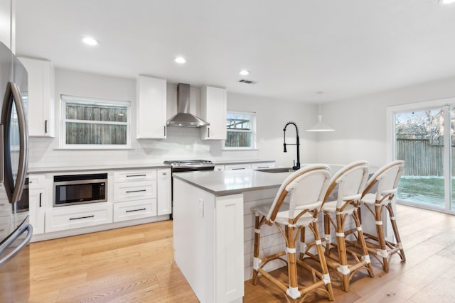 kitchen with wall chimney exhaust hood, a center island, stainless steel appliances, white cabinets, and sink