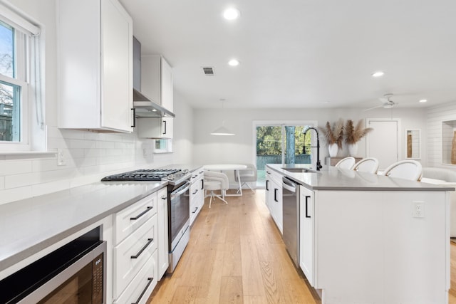 kitchen featuring a center island with sink, appliances with stainless steel finishes, pendant lighting, white cabinets, and sink