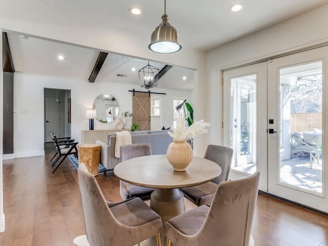 dining room with plenty of natural light, hardwood / wood-style flooring, a barn door, and beam ceiling