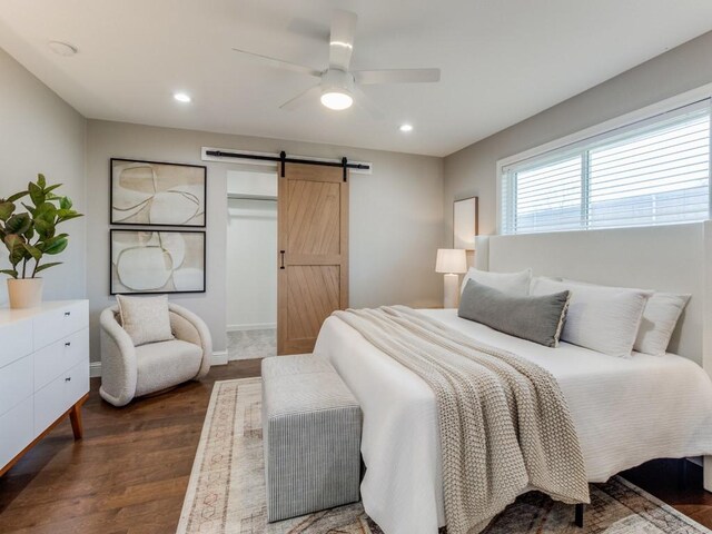 bedroom with ceiling fan, a barn door, and dark wood-type flooring