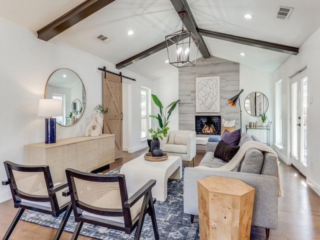 living room featuring an inviting chandelier, vaulted ceiling with beams, hardwood / wood-style floors, a healthy amount of sunlight, and a barn door