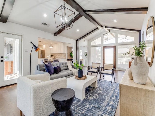 living room featuring a healthy amount of sunlight, hardwood / wood-style floors, an inviting chandelier, and lofted ceiling with beams