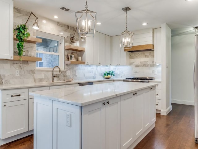 kitchen with light stone countertops, pendant lighting, a center island, white cabinets, and sink