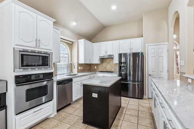 kitchen with stainless steel appliances, sink, a center island, light stone counters, and decorative backsplash