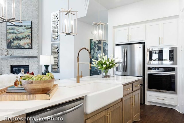 kitchen featuring stainless steel appliances, light stone countertops, a brick fireplace, white cabinetry, and decorative light fixtures