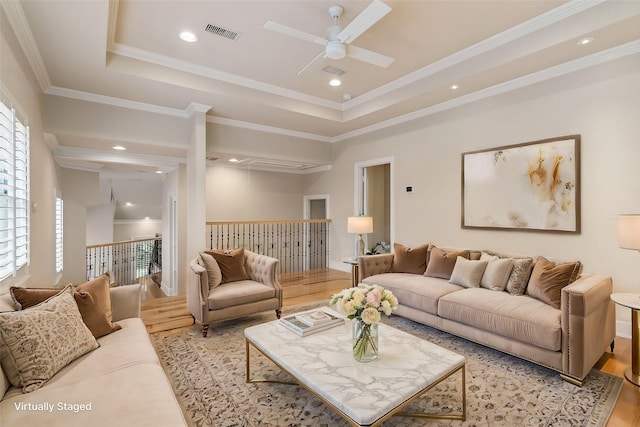 living room featuring light hardwood / wood-style floors, ceiling fan, a raised ceiling, and crown molding