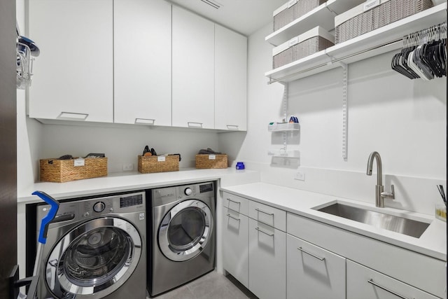 clothes washing area featuring light tile patterned floors, sink, washing machine and clothes dryer, and cabinets