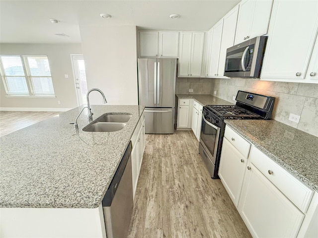 kitchen with light stone countertops, backsplash, white cabinets, appliances with stainless steel finishes, and sink