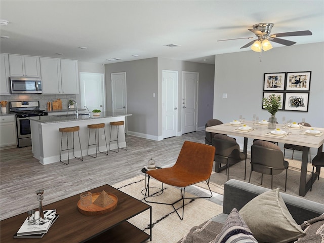 living room featuring light wood-type flooring, ceiling fan, and sink