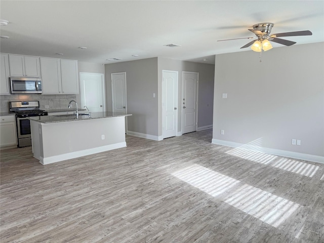 kitchen with white cabinets, light stone counters, tasteful backsplash, an island with sink, and appliances with stainless steel finishes