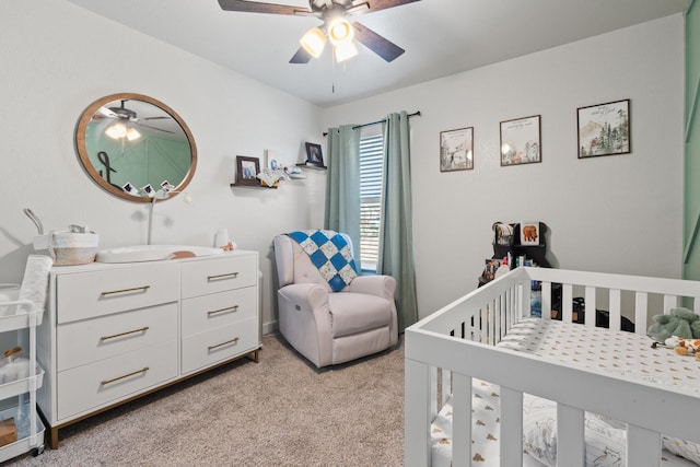 bedroom featuring a nursery area, ceiling fan, and light carpet