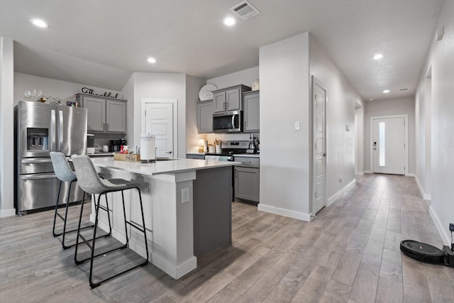 kitchen featuring a breakfast bar, stainless steel appliances, gray cabinetry, and a kitchen island with sink