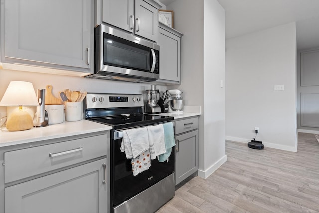 kitchen with appliances with stainless steel finishes, light hardwood / wood-style floors, and gray cabinets