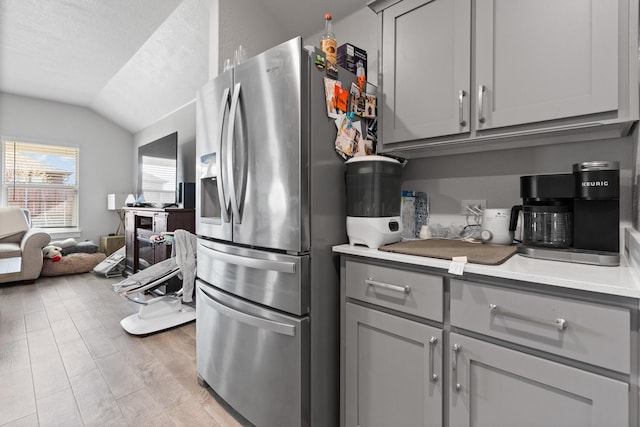 kitchen with vaulted ceiling, stainless steel fridge with ice dispenser, and gray cabinetry