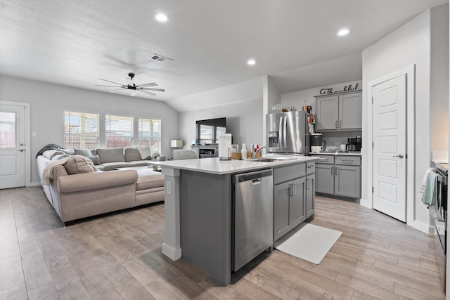 kitchen with stainless steel appliances, a center island with sink, vaulted ceiling, and gray cabinetry