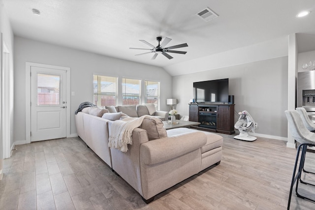 living room featuring ceiling fan, light hardwood / wood-style flooring, vaulted ceiling, and a fireplace