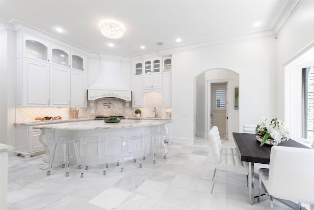 kitchen with white cabinets, a kitchen breakfast bar, premium range hood, light stone countertops, and a kitchen island