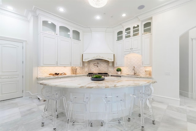 kitchen featuring sink, white cabinetry, light stone counters, custom exhaust hood, and a kitchen island