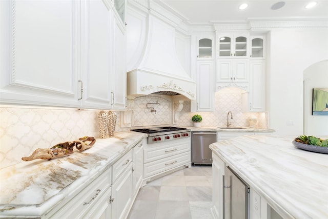 kitchen featuring light stone countertops, custom range hood, stainless steel gas cooktop, white cabinets, and sink