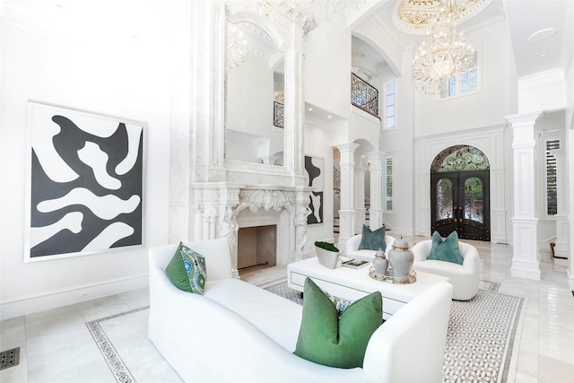 living room with a fireplace, decorative columns, french doors, a high ceiling, and a notable chandelier