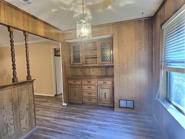 unfurnished dining area with a textured ceiling, dark hardwood / wood-style floors, wooden walls, an inviting chandelier, and crown molding