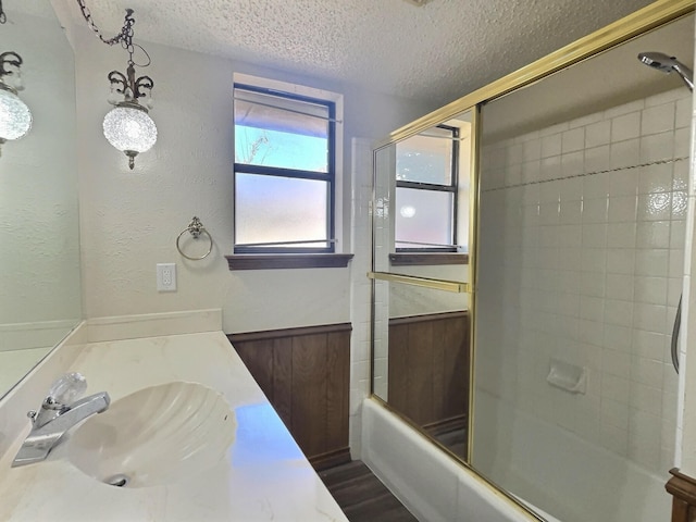 bathroom featuring a textured ceiling, wooden walls, hardwood / wood-style floors, bath / shower combo with glass door, and vanity