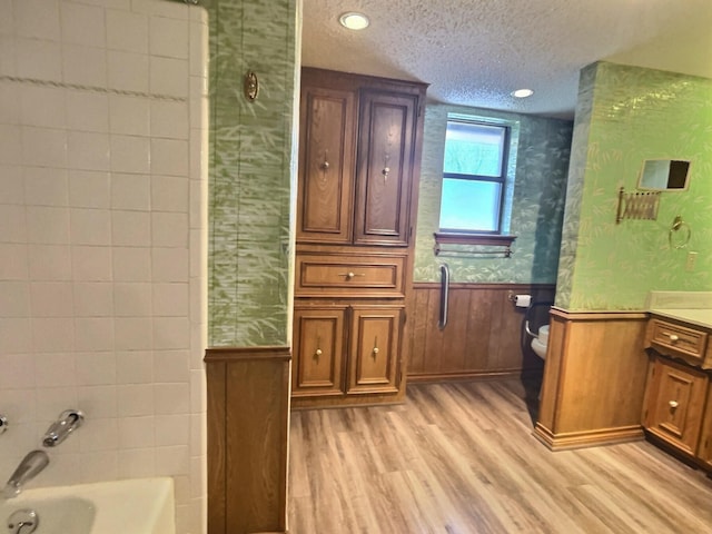 bathroom featuring a textured ceiling, hardwood / wood-style floors, toilet, wood walls, and vanity